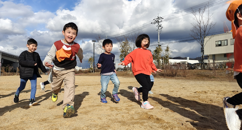 Happy children running in a field with their English teacher from Hoshida International.